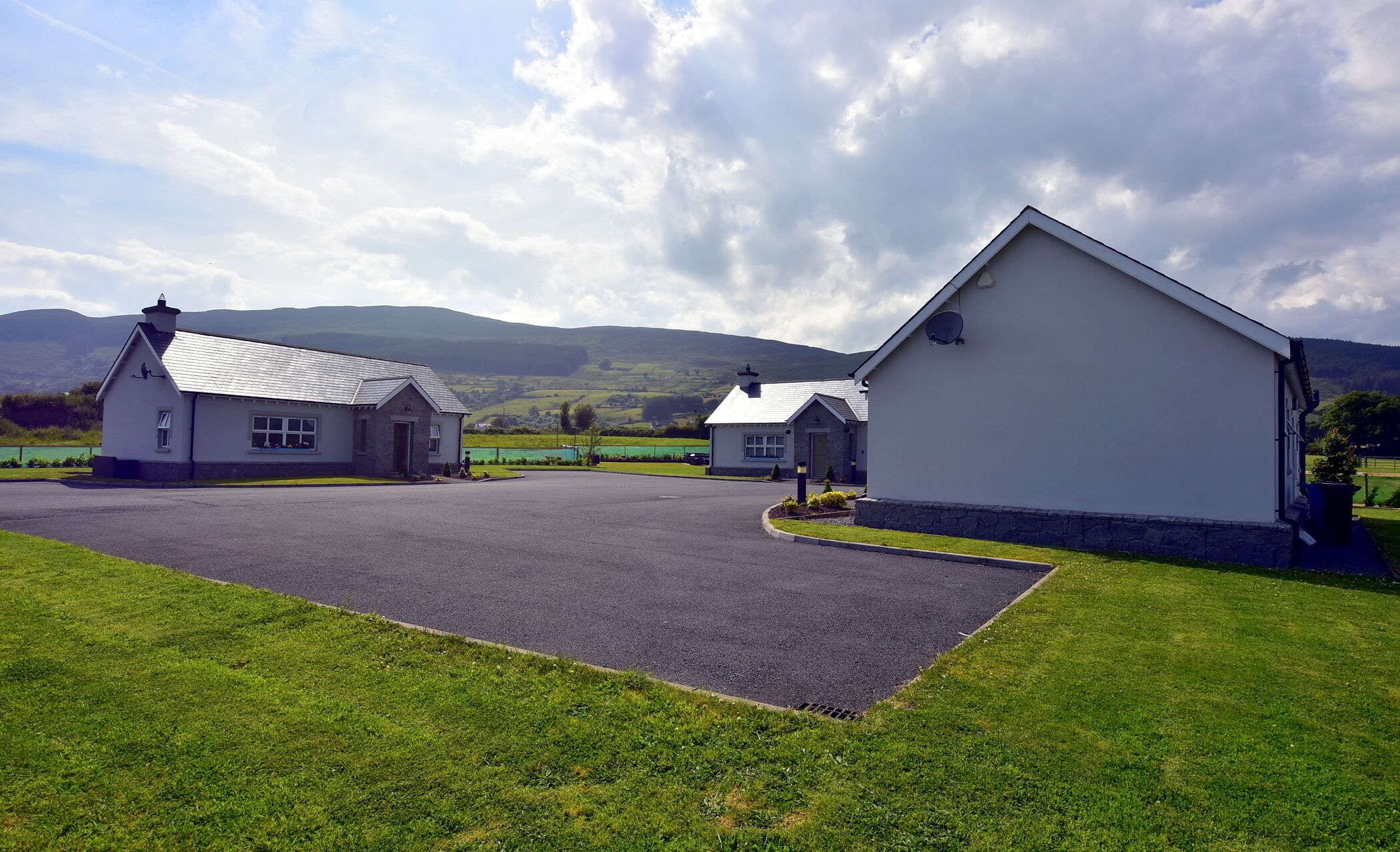 A property with a paved driveway, a grassy lawn, and a white building with a stone foundation.