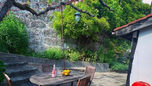 Une terrasse extérieure avec une table ronde, deux chaises, une bouteille et un saladier rempli de fruits.
