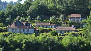 Un ensemble de maisons traditionnelles aux toits de tuiles rouges, nichées au milieu d’une végétation luxuriante et d’arbres.