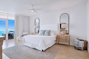 Une chambre spacieuse avec un grand lit, deux tables de chevet avec des lampes, un ventilateur de plafond et une vue sur l’extérieur grâce à une porte-fenêtre coulissante.