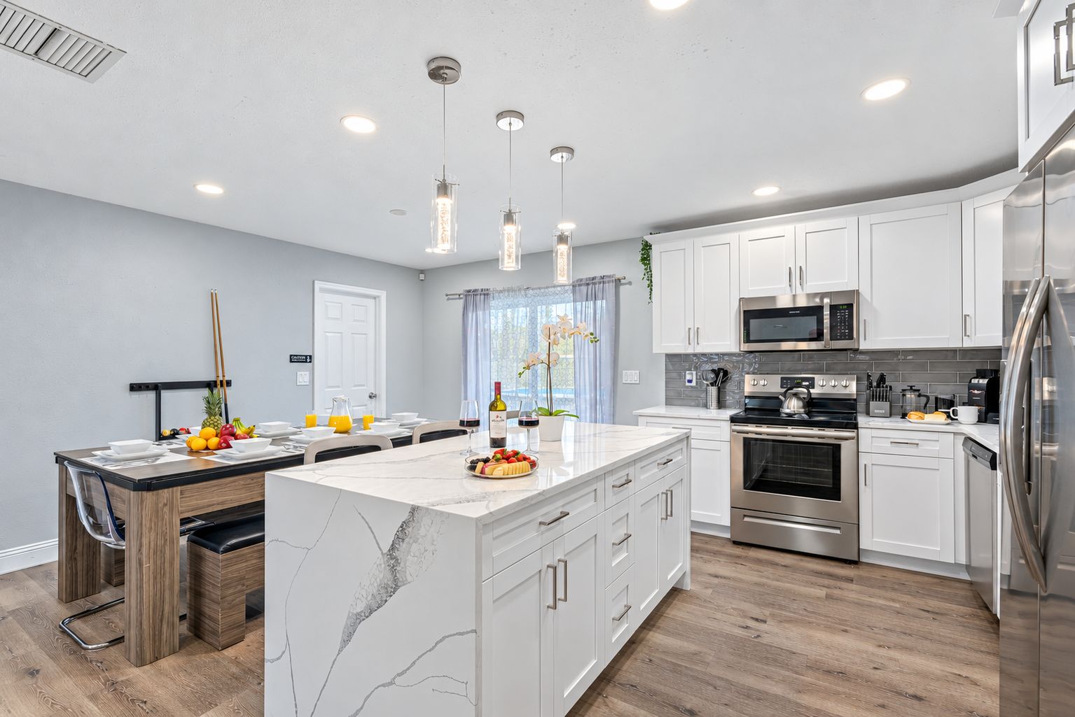 A modern kitchen with white cabinetry, stainless steel appliances, and a marble island.