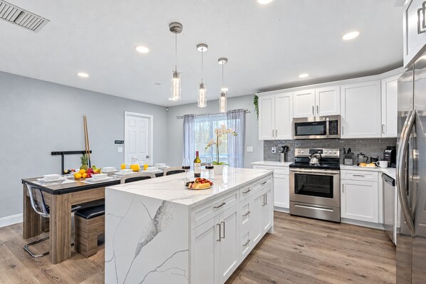 A modern kitchen with white cabinetry, stainless steel appliances, and a marble island.
