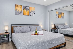 A modern hotel room with a large bed, bedside tables, a mirror, and artwork on the wall.