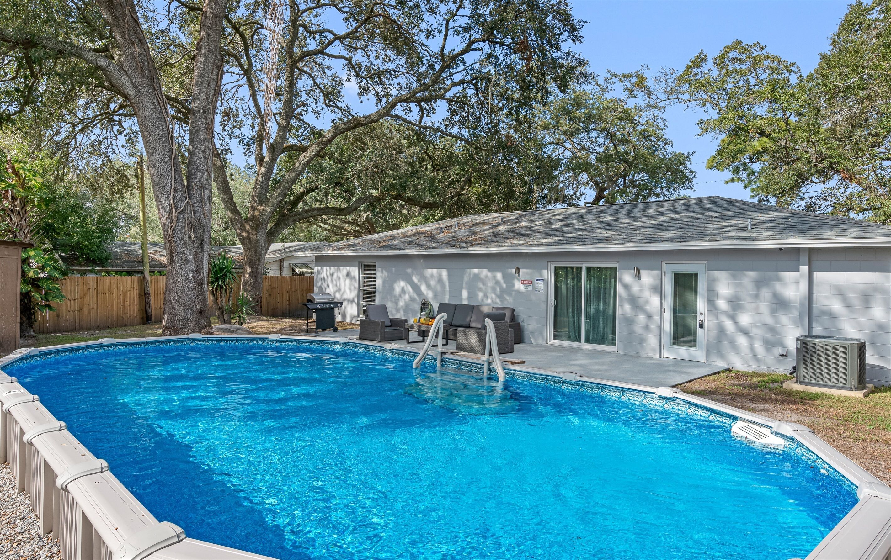 A swimming pool with a built-in deck, a barbecue grill, and a covered patio area with seating.