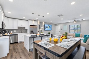A modern kitchen with white cabinetry, a central island, and a dining area with a wooden table.