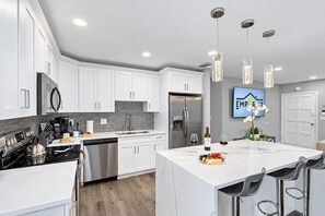 A modern kitchen with white cabinetry, stainless steel appliances, and a marble island with bar seating.