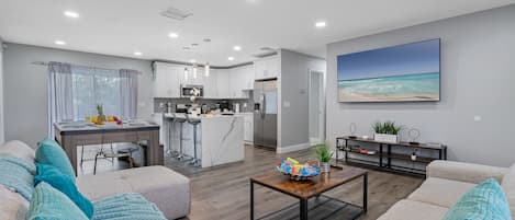 A modern living room with a sofa, coffee table, and a view of the kitchen and dining area.