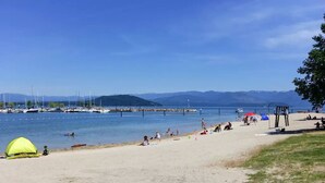 A beach with a tent, people relaxing, and boats in the background. - Downtown Sandpoint Lakeside Condo (Sandpoint)
