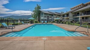 A swimming pool with lounge chairs, a building with balconies, and a mountainous backdrop. - Downtown Sandpoint Lakeside Condo (Sandpoint)