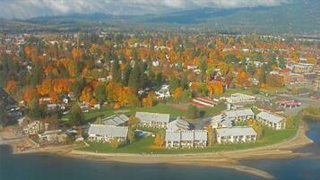 An aerial view of a coastal town with a marina, surrounded by autumn-colored trees and residential buildings.
