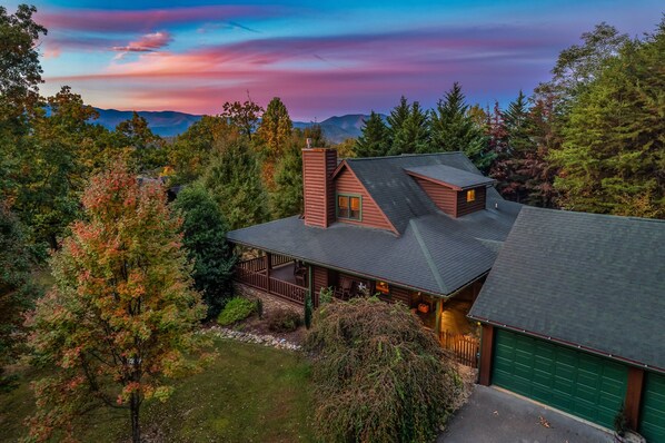 A cabin with a sloped roof, surrounded by trees and a mountain range in the background. - Spacious Family Cabin | 5 mi to National Park | Hot Tub | Arcade | Pool Access (Townsend)
