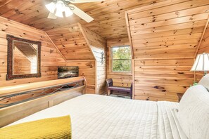 Un dormitorio de cabaña de madera con una cama, un aparador, un espejo y una ventana.