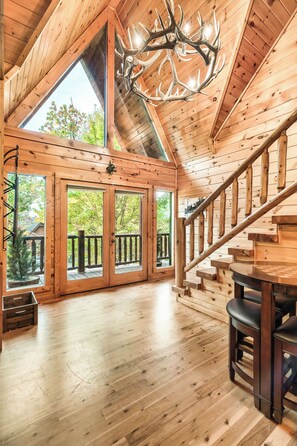 A spacious wooden interior with a high ceiling, a grand chandelier, and a staircase leading to an upper level. - Spacious Family Cabin | 5 mi to National Park | Hot Tub | Arcade | Pool Table (Townsend)