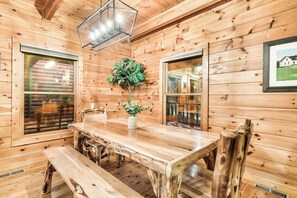 Un interior de madera con una mesa de comedor, sillas, una lámpara colgante y ventanas.