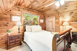A wooden cabin bedroom with a bed, bedside tables, a lamp, and a window.