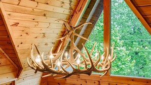 Un lampadario di corna appeso in una stanza in legno con una finestra vista su un paesaggio verde.