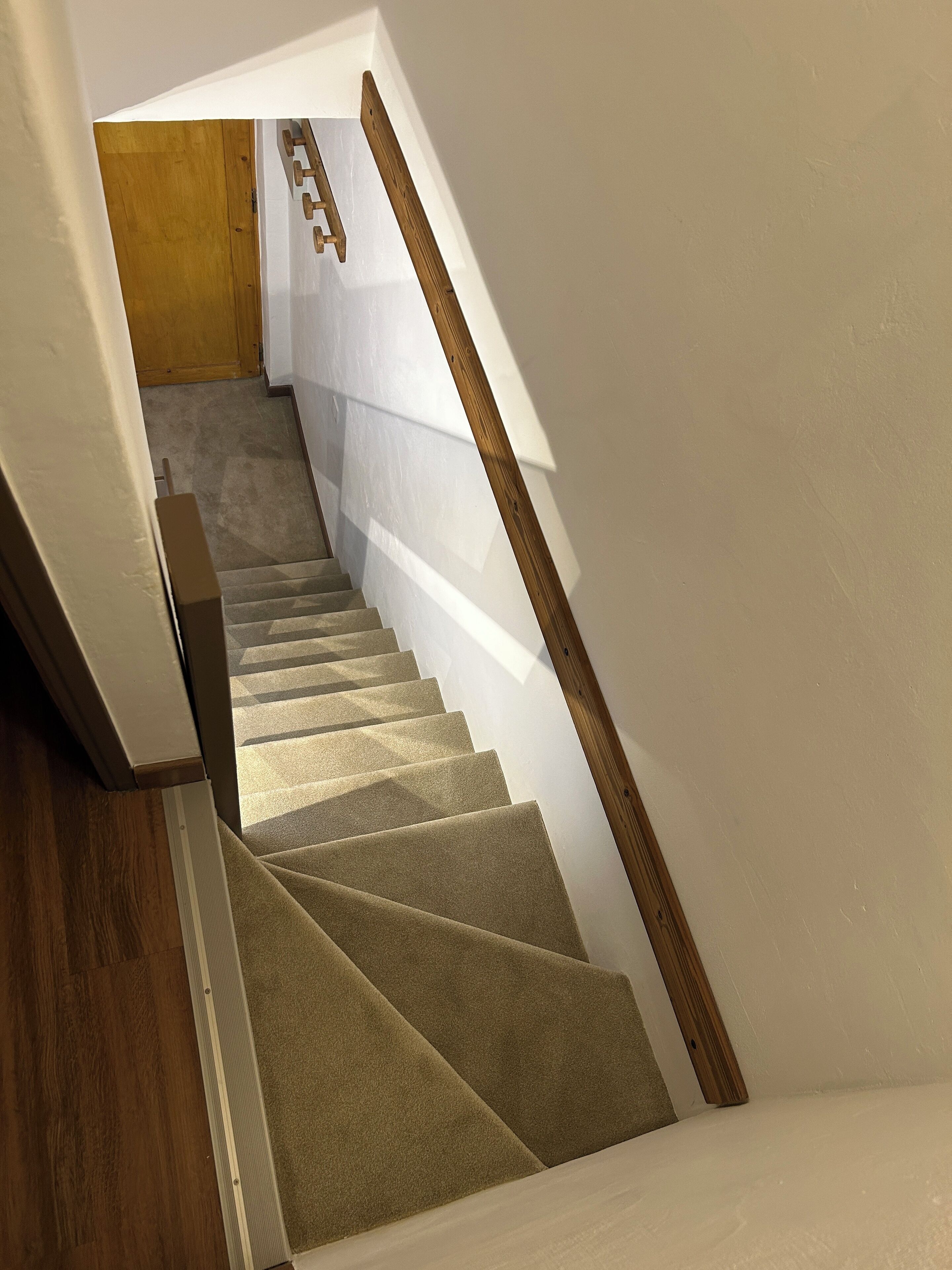 Un escalier avec des rampes en bois et des marches recouvertes de moquette, menant à un palier.