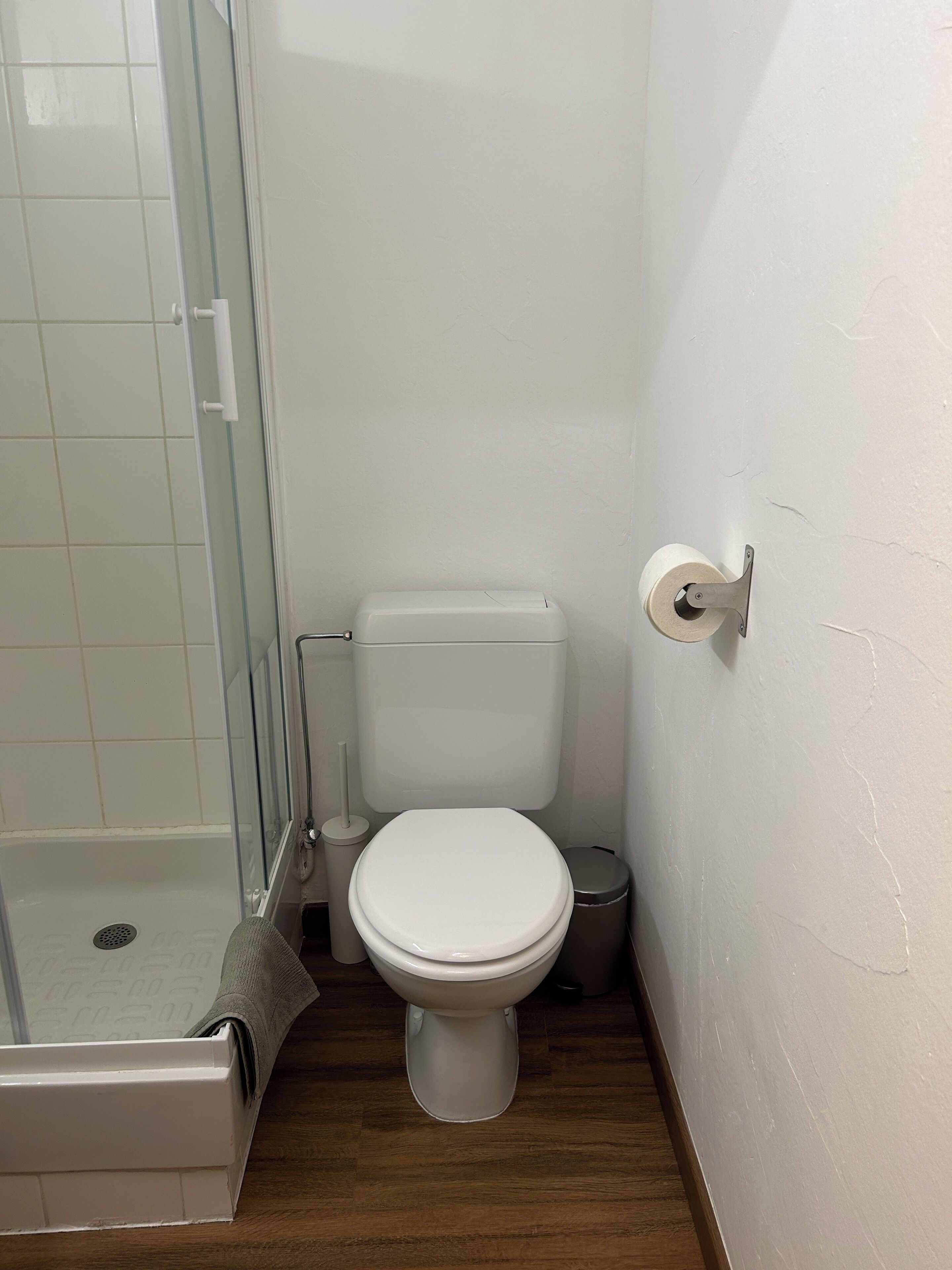 Ein kleines, kompaktes Badezimmer mit Toilette, einer Duschkabine aus Glas und einem Mülleimer.