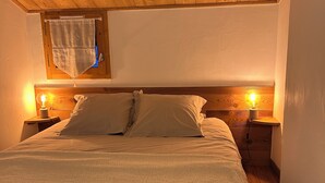 A bedroom with a wooden ceiling, a bed with a white textured blanket, two bedside lamps, and a window with a curtain.