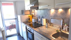 A compact kitchen with a dishwasher, oven, and a small countertop with a dish rack. - Appartement 2 Chambres Séparées Denviron 60m2 Anglet-plages (Anglet)