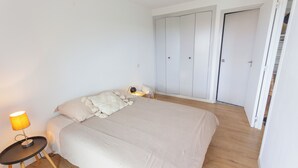 A bedroom with a bed, a bedside table with a lamp, and a wardrobe. - Appartement 2 Chambres Séparées Denviron 60m2 Anglet-plages (Anglet)