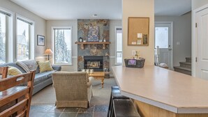 A cozy living room with a fireplace, a sofa, a coffee table, and a bar area. - Desirable Knoll Home with Hot Tub, BBQ, Laundry - Open Den with Sofa Bed (Silver Star Mountain)