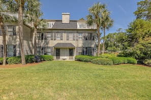 Traditional architecture surrounds a central entrance, flanked by palm trees, amidst well-maintained gardens.