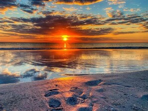 Atardecer sobre una playa con huellas en la arena.