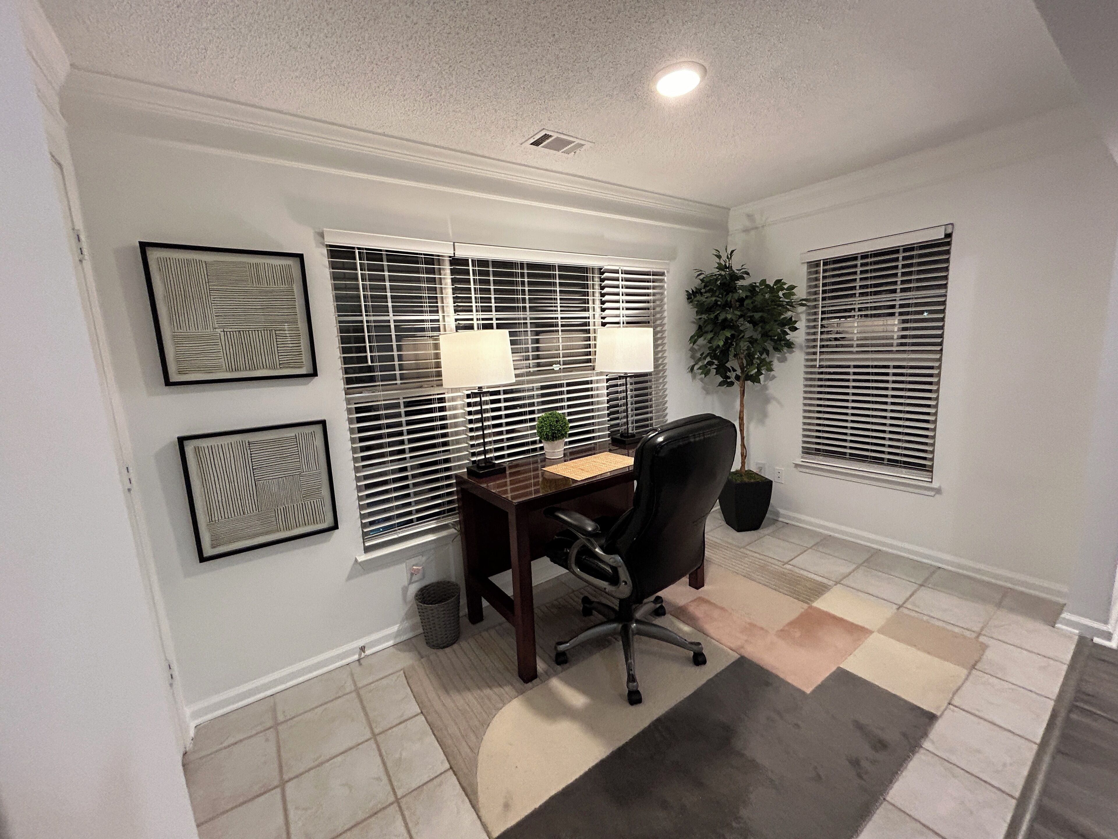 A home office with a desk, two lamps, a chair, and a potted plant.
