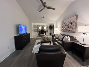 A modern living room with a flat-screen TV, a leather sofa, a coffee table, and a ceiling fan. - Fully Furnished One Bedroom/ One Bath In Alpharetta (Alpharetta)