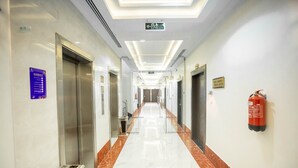 Un couloir d’hôtel avec un sol en marbre, des ascenseurs et un extincteur fixé au mur.