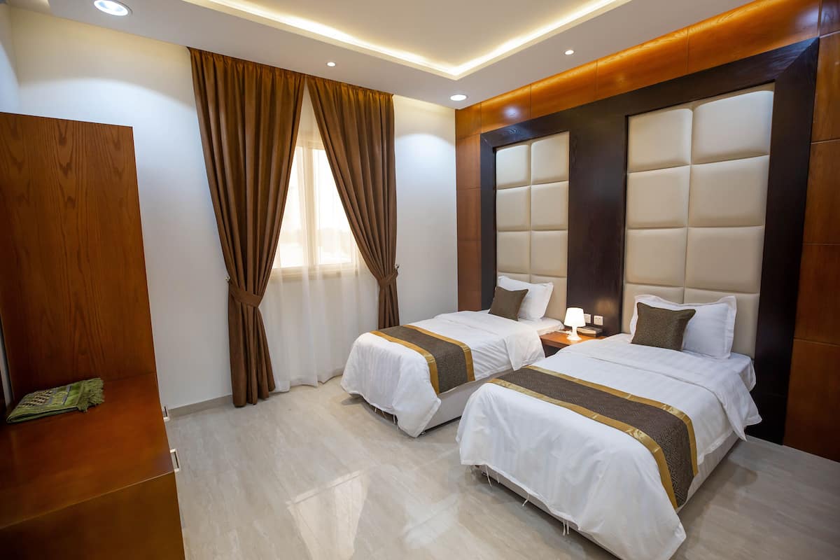A hotel room with two beds, wooden paneling, a nightstand, and a window with curtains.