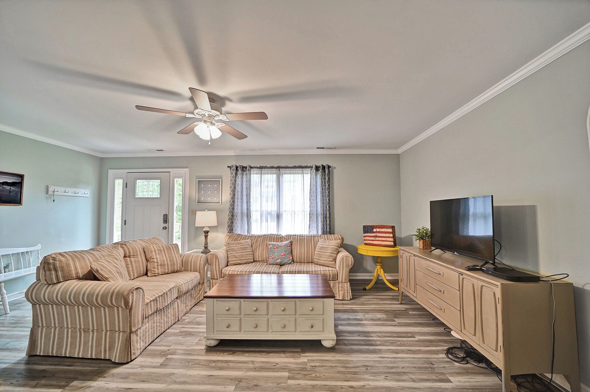 A living room with striped sofas, a coffee table, a TV, and a ceiling fan.