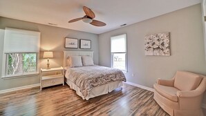 Ein Schlafzimmer mit Bett, Nachttisch, Sessel, Deckenventilator und Bildern an den Wänden.