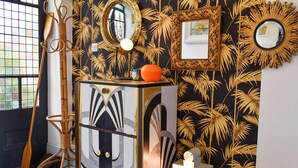 A room with a checkered floor, a decorative cabinet, a wicker chair, and a wall with a tropical leaf pattern. - 4 bedroom accommodation in Harwich (Harwich)
