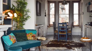 A cozy living room with a teal sofa, a dining table with chairs, a large plant, and a cowhide rug. - 4 bedroom accommodation in Harwich (Harwich)