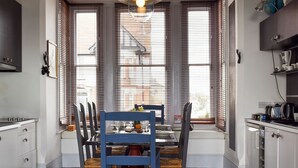 A dining area with a table set for four, a blue chair in the foreground, and a kitchen area with a stove and cabinets. - 4 bedroom accommodation in Harwich (Harwich)