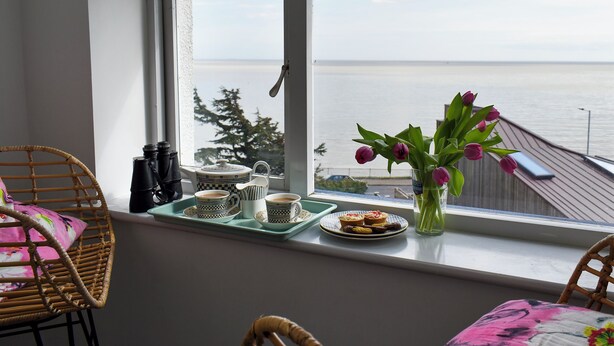 A balcony with a view of the sea, a wicker chair, a table with a tray holding cups and pastries, and a vase with flowers. - 4 bedroom accommodation in Harwich (Harwich)