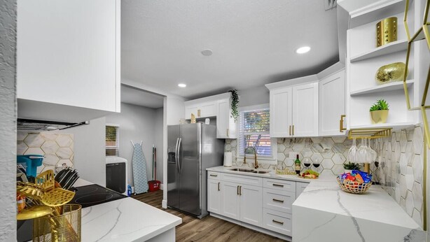 Una cocina moderna con armarios blancos, un refrigerador de acero inoxidable y piso de madera.