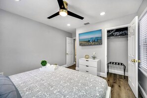 Une chambre à coucher comprenant un lit, un ventilateur de plafond, une commode, une table de chevet et un placard.
