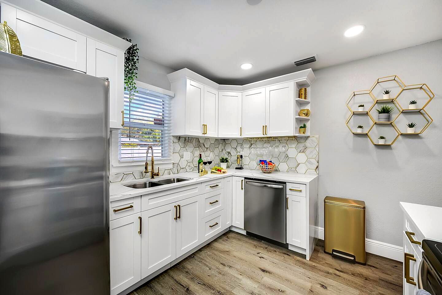 A modern kitchen with white cabinets, a stainless steel refrigerator, and a wooden floor.