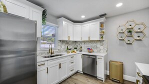 Una cocina moderna con armarios blancos, un refrigerador de acero inoxidable, un lavavajillas y piso de madera.