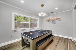 Une pièce avec une table de ping-pong, une fenêtre avec des stores et des œuvres d’art accrochées au mur.