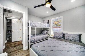 Un dormitorio con literas, un ventilador de techo, una mesita de noche con lámpara y una ventana con persianas.