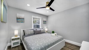 Un dormitorio con cama, mesitas de noche, ventilador de techo y ventana con persianas.