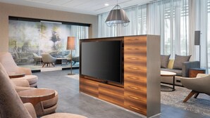 Un moderno vestíbulo de hotel con un televisor de pantalla plana grande, asientos cómodos y un ventanal con cortinas traslúcidas.