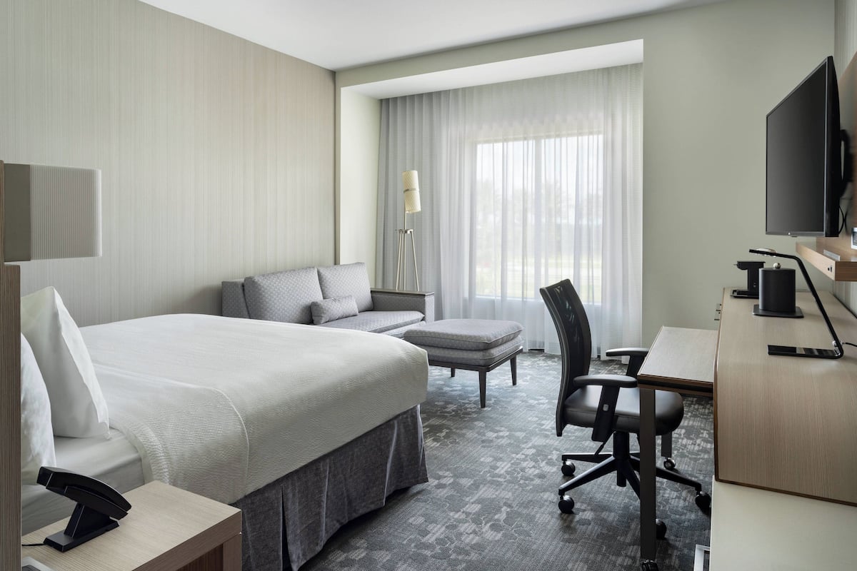 Una habitación de hotel con una cama grande, un escritorio, una silla, una lámpara y un televisor.