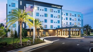 Un hotel Courtyard by Marriott de diseño moderno, con una entrada bien iluminada y un área ajardinada con palmeras.