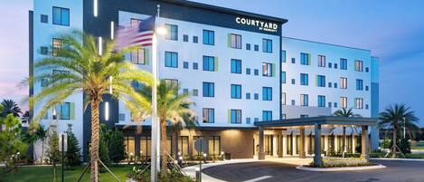 A Courtyard by Marriott hotel with a modern design, featuring a well-lit entrance and a landscaped area with palm trees.