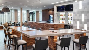 Un moderno vestíbulo de hotel con una gran mesa central, zona de bar y asientos.